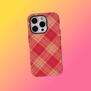 May include: A red and peach plaid phone case. The case has a black border and a camera cutout. The plaid pattern is a diagonal design. The background is a gradient of yellow, orange, and pink.