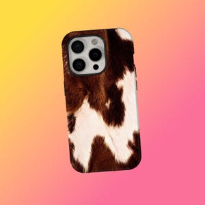 May include: A smartphone case with a cowhide design in brown and white. The case has a glossy finish and a black camera module. The pattern resembles natural animal fur.