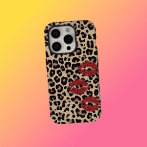Pode incluir: Uma capa de telefone com um design de estampa de leopardo em bege e preto. A capa apresenta três marcas de beijos vermelhos. A capa foi projetada para um smartphone.