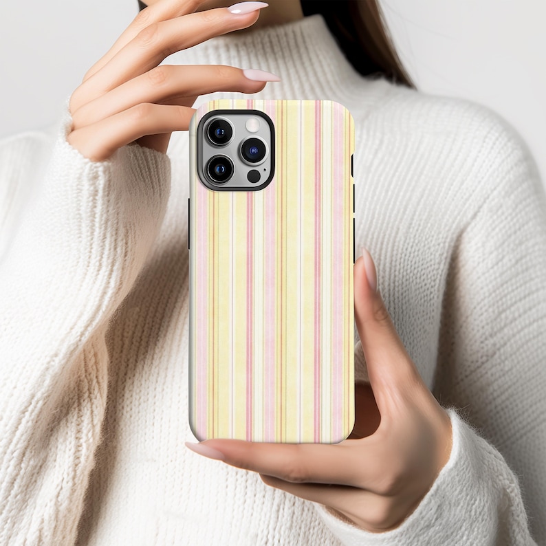 May include: A smartphone case with a vertical striped pattern in pastel yellow, pink, and white. The case has a black border and is held in a person's hands. The case is designed to fit a modern smartphone.