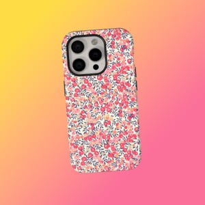 Peut inclure: Coque de téléphone à motif floral. Le motif présente de petites fleurs roses et rouges avec des feuilles vertes sur fond blanc. La coque a un bord noir et une découpe pour l'appareil photo. Conçu pour un smartphone.