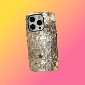 Op de afbeelding: Een telefoonhoesje met een mozaïekontwerp. De hoes is bedekt met kleine, rechthoekige stukjes in goud- en zilverkleuren, waardoor een textuuroppervlak ontstaat. Verschillende stervormige uitsparingen zijn zichtbaar op het onderste deel.