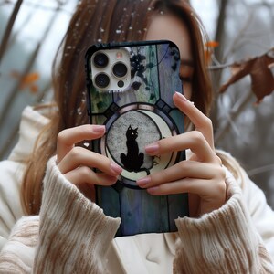 Puede incluir: Una funda de tel&eacute;fono con la silueta de un gato negro sobre una luna creciente. El dise&ntilde;o est&aacute; sobre un fondo de estilo vidriera en tonos azules, verdes y morados. La funda tiene un parachoques protector y recortes para la c&aacute;mara.