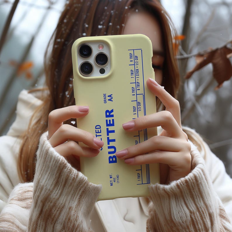 May include: A light yellow phone case with the word "BUTTER" in blue and white text. The case has a butter-themed design with measurements in tablespoons and cups. The case also has the text "NET WT. 4 OZ (113G)" and "GRADE AA".