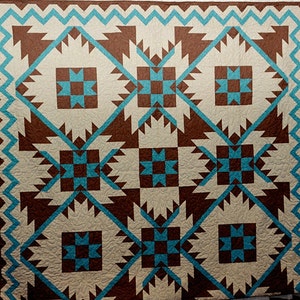 May include: A quilt with a geometric pattern in shades of brown, teal, and cream. The quilt is made up of squares and triangles, and the pattern is repeated throughout the quilt.
