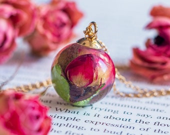 May include: A gold chain necklace with a round pendant featuring a preserved pink rose encased in clear resin.