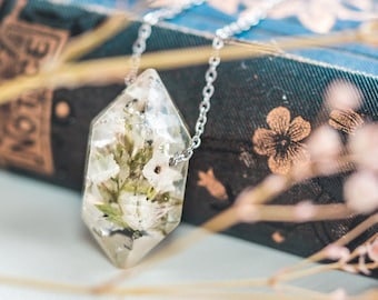 May include: A silver chain necklace with a clear, faceted pendant containing pressed white flowers and green leaves.