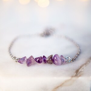 Peut inclure: Un bracelet délicat en chaîne argentée avec une rangée de petites pierres d'améthyste violettes.