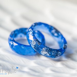 Peut inclure: Deux bagues en résine bleue avec des paillettes argentées incrustées dans la résine. Les bagues sont empilées l'une sur l'autre.