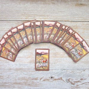 May include: A set of rectangular playing cards arranged in a fan shape with one card placed vertically in the center. Each card features a printed illustration of a red fox standing in a field with yellow trees, green grass, and brown hills.