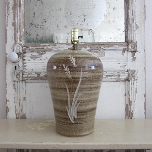 May include: A ceramic table lamp with a brown and beige striped pattern and a white floral design. The lamp has a brass-colored socket and a rounded, vase-like shape. The lamp is approximately 12 inches wide and 20 inches tall.