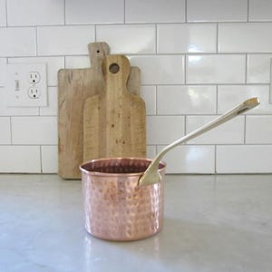 May include: A set of three ceramic mugs with a speckled, matte finish. The mugs are in shades of cream, light brown, and dark brown. Each mug has a simple, minimalist design, perfect for coffee or tea.