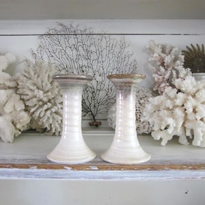 May include: Two off-white ceramic candle holders with a spiral design. The candle holders have a flared base and a brown rim. The background includes white coral and a black coral-like decoration.