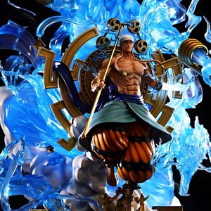 May include: A detailed figurine of a muscular character with a staff, wearing a white head covering and blue clothing. The figure is surrounded by translucent blue energy effects and a golden wheel-like structure. The base features a golden structure and the name "ENEL".