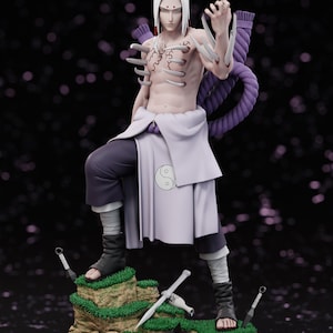 以下が含まれることがあります： 小さな草のプラットフォームに立っている、白い髪のキャラクターの精巧なフィギュア。フィギュアは上半身裸で、濃い色のズボンと明るい色のラップを着用しています。紫色のロープといくつかの武器を持っています。