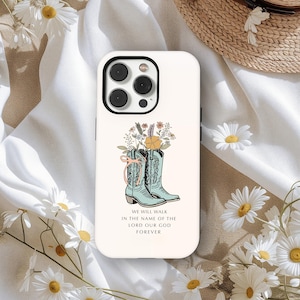 Op de afbeelding: Een witte telefoonhoes met een ontwerp van lichtblauwe cowboylaarzen en een bloemstuk. De laarzen zijn versierd met een roze strik. De tekst luidt: "WIJ ZULLEN WANDELEN IN DE NAAM VAN DE HEER ONZE GOD VOOR ALTIJD".