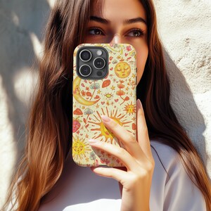 May include: A phone case with a whimsical design featuring suns, moons, stars, and other celestial and floral elements in shades of yellow, orange, and red on a cream background. The case has a glossy finish and a camera cutout.