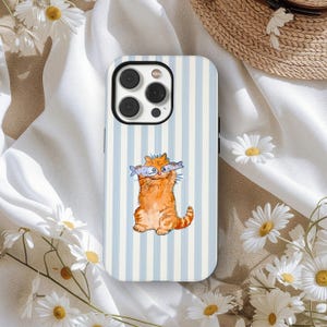 May include: A phone case with a light blue and white striped design. The case features a watercolour illustration of an orange cat holding two fish. The phone case has a black camera module.