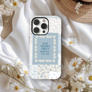 May include: A phone case with a patchwork design in light blue and white floral patterns. The center features a light blue square with the text "IN HIS PRESENCE THERE IS fullness OF JOY" in a floral frame.
