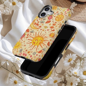 May include: A black smartphone with a decorative case featuring a whimsical design. The case has a cream-colored background with illustrations of smiling suns, moons, stars, and flowers in shades of orange, red, and yellow.