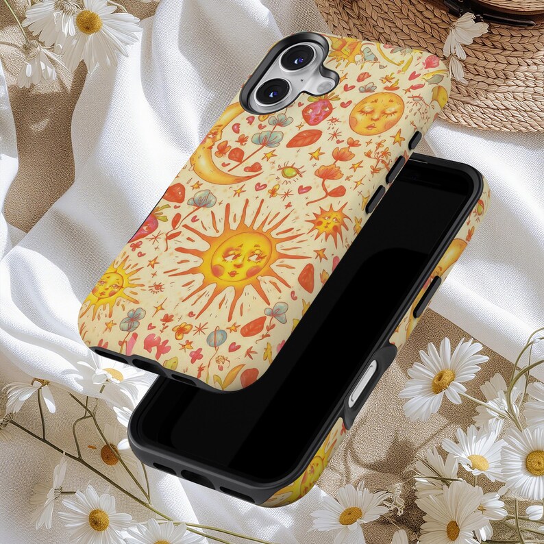 May include: A black smartphone with a decorative case featuring a whimsical design. The case has a cream-colored background with illustrations of smiling suns, moons, stars, and flowers in shades of orange, red, and yellow.