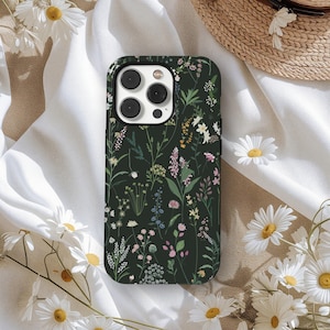Op de afbeelding: Een donkergroene telefoonhoes met een bloemenpatroon met verschillende wilde bloemen in wit, roze, geel en blauw. De hoes heeft een glanzende afwerking en een camera-uitsparing. Madeliefjes zijn rond de hoes verspreid.