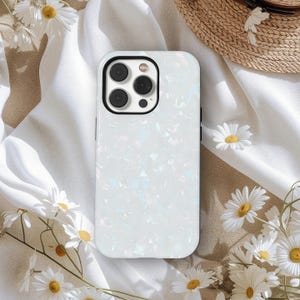 May include: White pearlescent phone case with a textured surface. The case has a black camera ring and buttons. Daisies and a straw hat are in the background.
