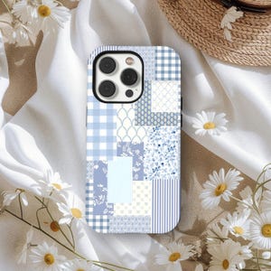 Pode incluir: Uma capa de smartphone com um design de patchwork em vários tons de azul e branco. A capa apresenta uma mistura de padrões, incluindo xadrez, floral e listras. A capa do telefone tem um módulo de câmera preto.