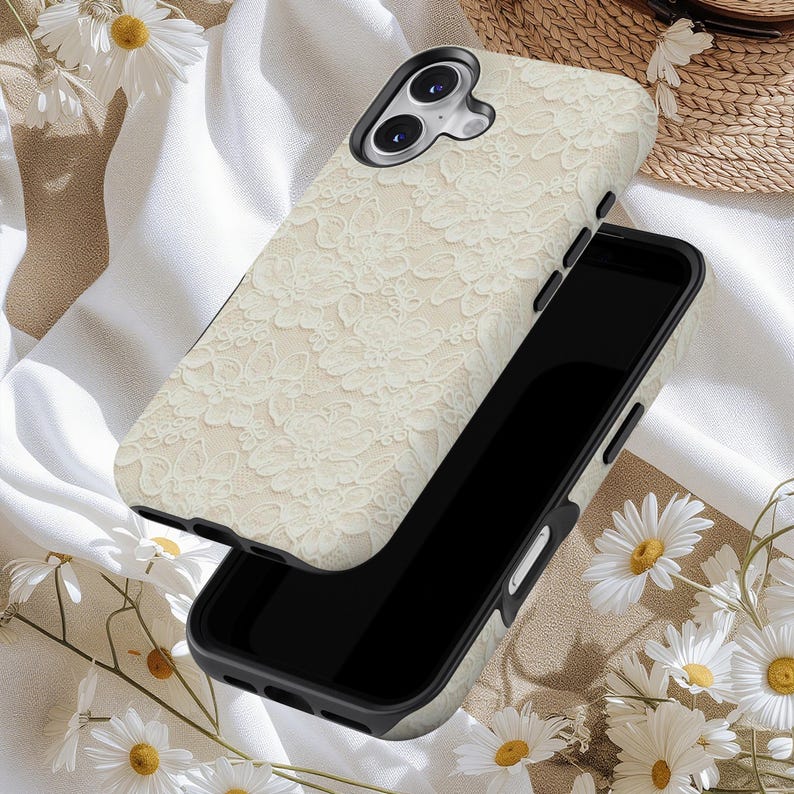 Puede incluir: Una funda de tel&eacute;fono color crema con un delicado dise&ntilde;o de encaje se muestra sobre un tel&eacute;fono inteligente negro. La funda tiene un dise&ntilde;o en relieve y un acabado mate. El fondo incluye tela blanca, margaritas y un sombrero de paja.