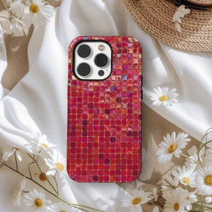 May include: A red and pink mosaic-patterned phone case. The case has a square tile design with varying shades of red and pink. The phone case has a black border and a camera cutout.