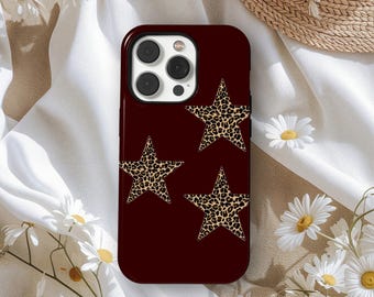May include: A maroon phone case featuring three leopard print stars. The case has a glossy finish and a camera cutout. The background is a white fabric with daisies and a straw hat.