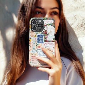 May include: A floral phone case with various inspirational quotes and phrases. The case features a collage of flowers, mountains, and text, including "grace," "let your light shine," and "God is Good." The case is designed to fit a smartphone.