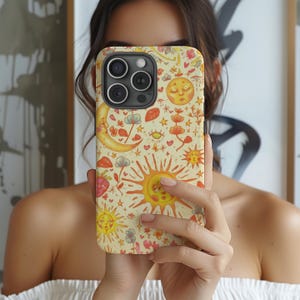 May include: A phone case with a whimsical celestial design. The case features a repeating pattern of suns, moons, stars, flowers, and hearts in shades of yellow, orange, red, and blue on a cream background. The phone case has a camera cutout.