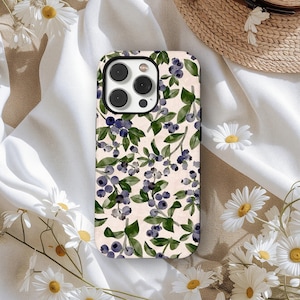Puede incluir: Funda de teléfono con un diseño de acuarela de arándanos y hojas verdes sobre un fondo beige claro. La funda tiene un acabado brillante y un recorte para la cámara. El diseño se repite en toda la superficie de la funda.