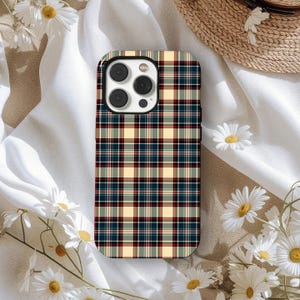 May include: A smartphone case featuring a tartan design in red, navy, and cream. The case has a black border around the camera lenses. White daisies and a straw hat are in the background.