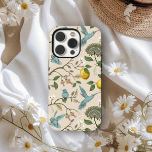Könnte beinhalten: Eine Handyhülle mit beigem Hintergrund und botanischem Design. Das Design umfasst blaue Kolibris, gelbe Zitronen, grüne Blätter und florale Elemente. Die Hülle hat eine glänzende Oberfläche und einen Kameraausschnitt.