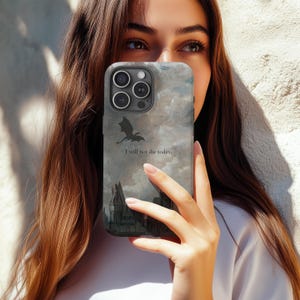 Op de afbeelding: Een smartphonehoesje met een fantasiethema. De hoes heeft een draak-silhouet, een kasteelillustratie en de tekst "I will not die today." De achtergrond heeft een wolkachtig, aquarelachtig effect in grijstinten en blauw.