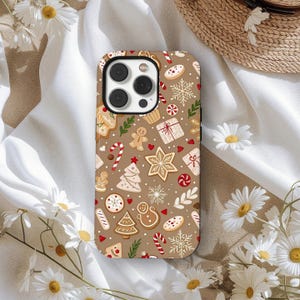 May include: A phone case with a brown background and a repeating pattern of Christmas cookies. The cookies include gingerbread men, snowflakes, candy canes, and Christmas trees. The case has a black camera module.