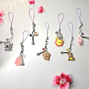 May include: A collection of decorative cell phone charms with various animal and object designs. Each charm features a small, colorful figurine attached to a silver-tone microphone and a purple loop. The charms include a koala, pig, squirrel, duck, bear, and bunny.