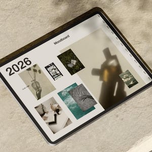 Op de afbeelding: Een digitale tablet met een moodboard voor 2026. Het scherm toont een collage van afbeeldingen, waaronder een vaas met planten, een boek op gras en water. De tablet heeft een donkerbruine rand en ligt op een lichtgekleurd oppervlak.