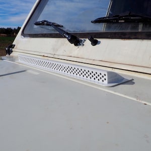 Puede incluir: Un vehículo blanco con un limpiaparabrisas negro y una ventilación de plástico blanco en el capó.