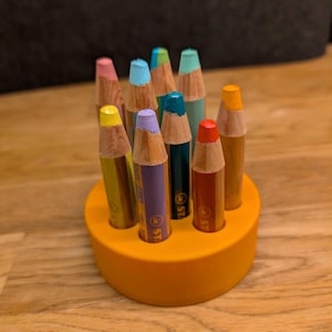 Könnte beinhalten: Ein gelber Bleistifthalter mit einer Auswahl an bunten Bleistiften, darunter Gelb, Grün, Blau, Lila, Rot und Orange.