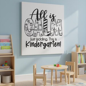 May include: A white canvas with the text "All is CALM Just kidding. This is Kindergarten!" in black. The word "CALM" is decorated with snowflakes, a reindeer, a snowman, and Christmas lights. A small wooden table and chairs are in front of the canvas.