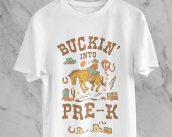 May include: White t-shirt with a cowboy-themed graphic. The design features a cowboy riding a bucking horse, with the text "BUCKIN' INTO PRE-K" in brown lettering. Additional cowboy-related icons are included in the design.