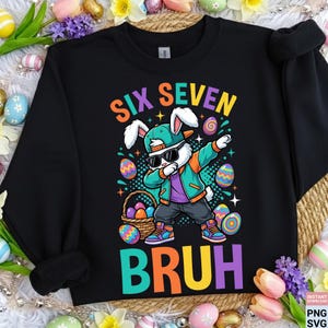 Może przedstawiać: Czarna bluza z kolorową grafiką zajączka wielkanocnego w pozie dab, w okularach przeciwsłonecznych i czapce. Tekst "SIX SEVEN BRUH" znajduje się nad i pod królikiem. Wzór zawiera pisanki i koszyk z jajkami.