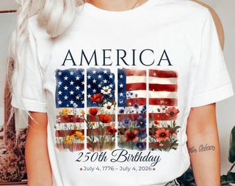 Może przedstawiać: Biała koszulka z patriotycznym wzorem. Koszulka zawiera napis "AMERICA" nad stylizowaną amerykańską flagą z kwiatowymi akcentami. Poniżej napis "250th Birthday" z datami "July 4, 1776 - July 4, 2026".
