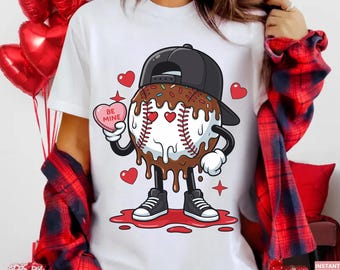May include: White t-shirt featuring a cartoon baseball character with a chocolate glaze, sprinkles, and a black cap. The baseball holds a pink heart-shaped candy that says "BE MINE". Red hearts and stars surround the baseball.