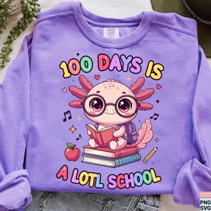 May include: A lilac Comfort Colors sweatshirt featuring a colorful graphic. The graphic includes an axolotl wearing glasses and reading a book, with the text "100 DAYS IS A LOTL SCHOOL" in a playful font. Additional elements include musical notes, hearts, and a pencil.