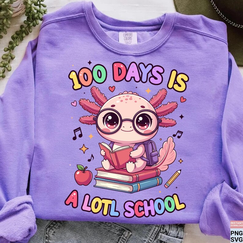 May include: A lilac Comfort Colors sweatshirt featuring a colorful graphic. The graphic includes an axolotl wearing glasses and reading a book, with the text "100 DAYS IS A LOTL SCHOOL" in a playful font. Additional elements include musical notes, hearts, and a pencil.