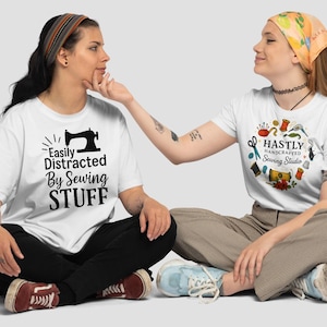 Puede incluir: Dos mujeres con camisetas blancas con gráficos de costura. Una camiseta dice "Easily Distracted By Sewing STUFF" con una ilustración de máquina de coser. La otra camiseta dice "Hastly Handcrafted Sewing Studio" con herramientas de costura.